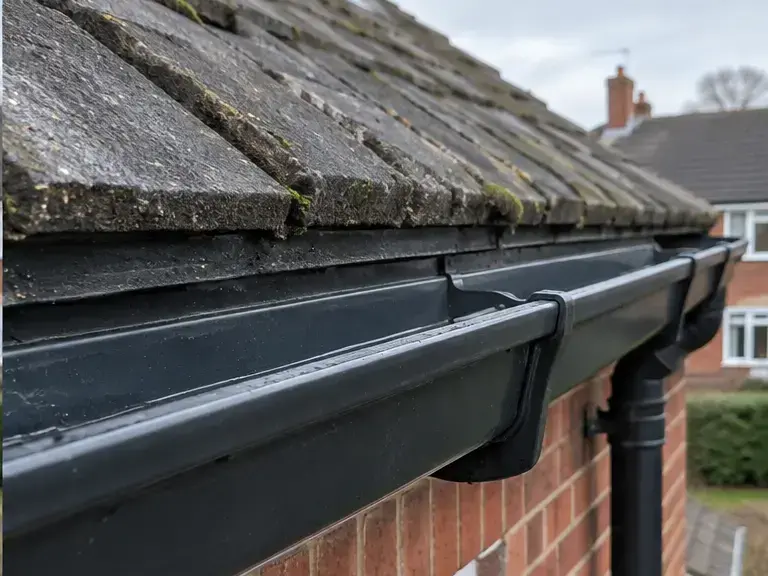 Clean black gutter after debris removal on a red-brick UK house